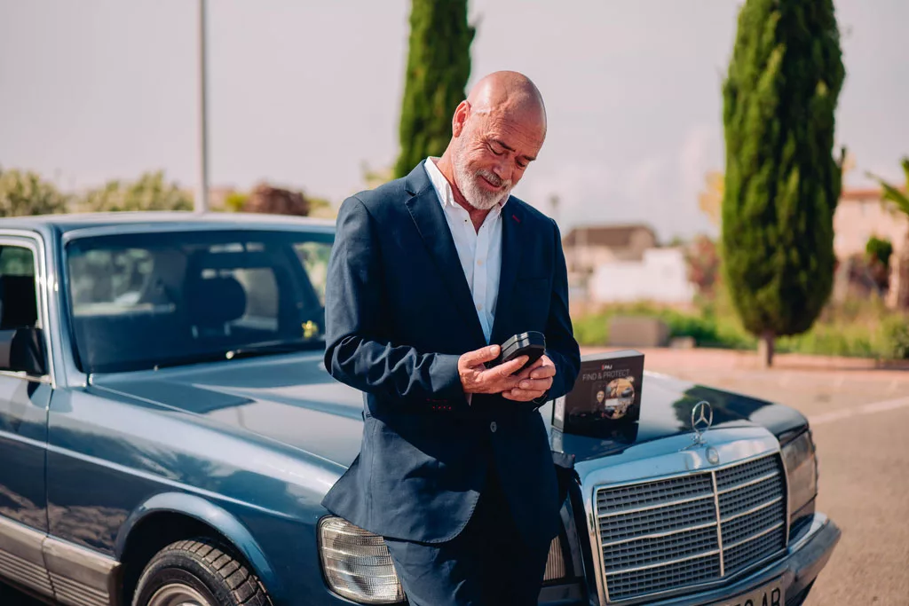 Mann vor seinem Mercedes Benz Oldtimer mit einem GPS Tracker von PAJ in der Hand